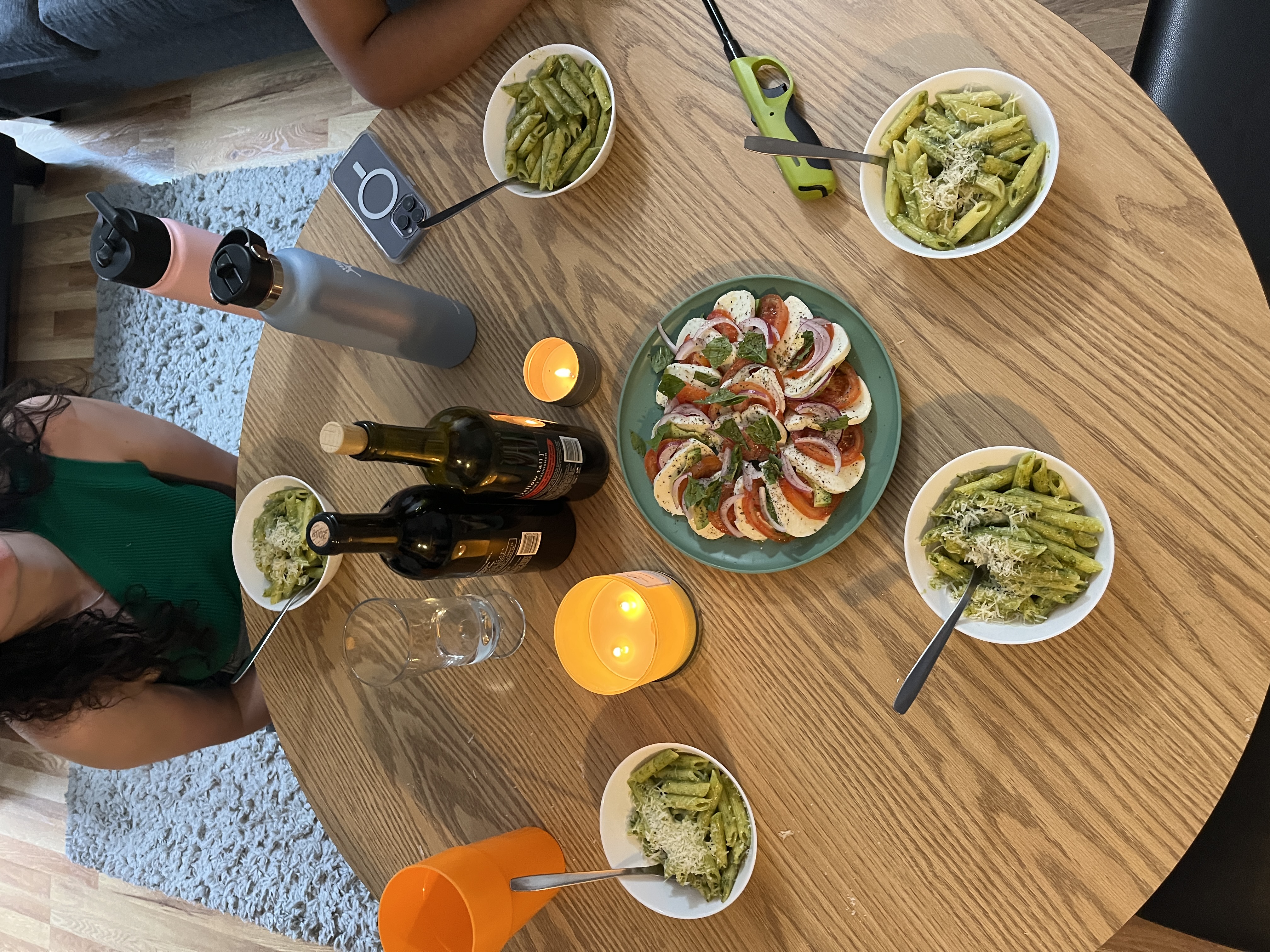 Dinner is served on a round table with pesto pasta in white bowls.